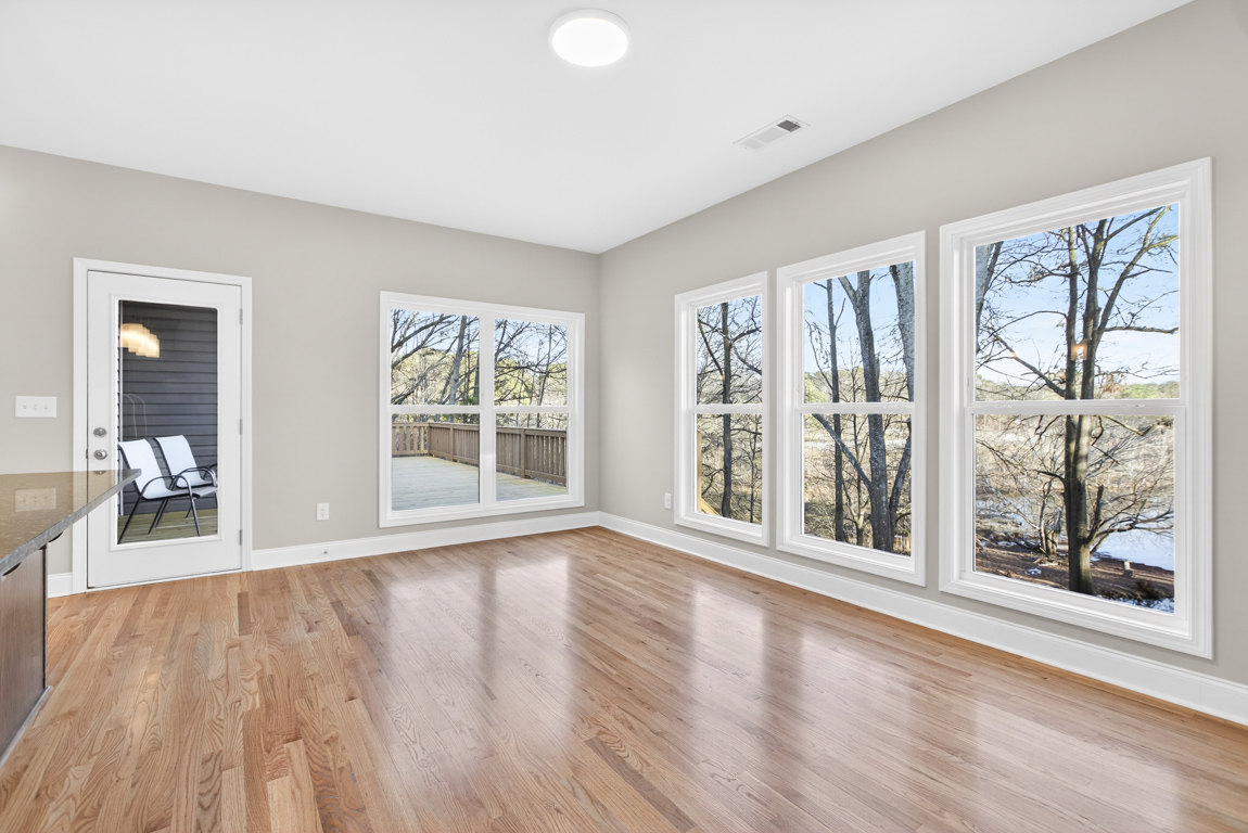 Hardwood floor in a bright room with large windows, white chair on a porch outside, deck and trees visible through the glass