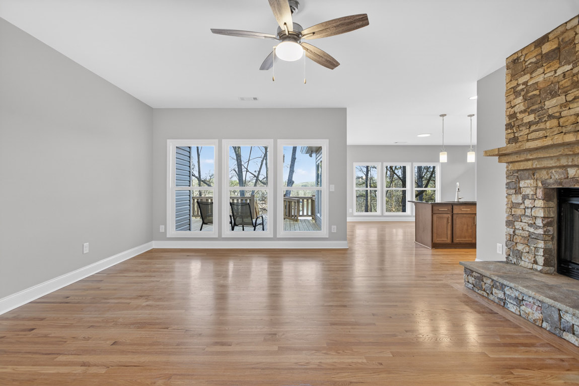 Living room with hardwood floors, white fireplace, ceiling fan with light, large windows overlooking deck with outdoor chair