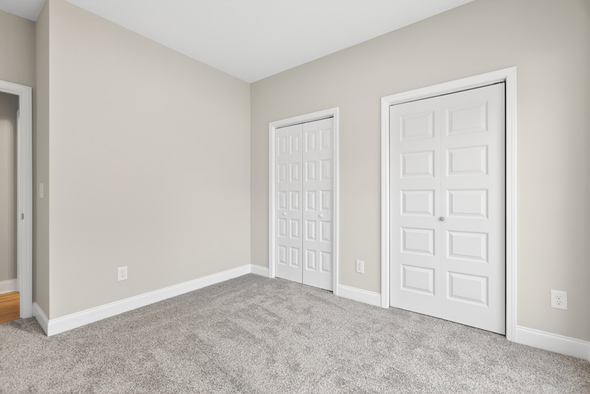 Grey-walled room with white ceiling, carpeted floor and white trim, featuring two white doors—one with a silver handle and one with a black handle.