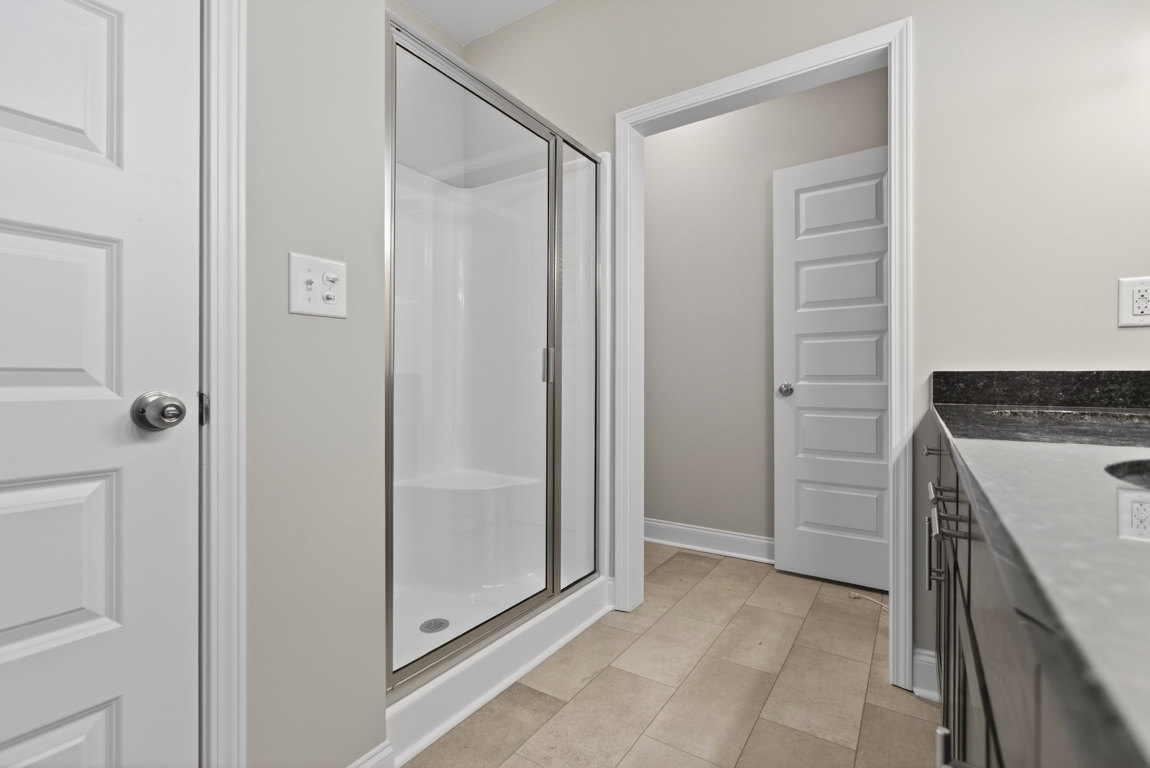 Modern bathroom featuring a glass-enclosed shower, white ceramic sink with chrome faucet, light gray tile flooring, and white cabinetry