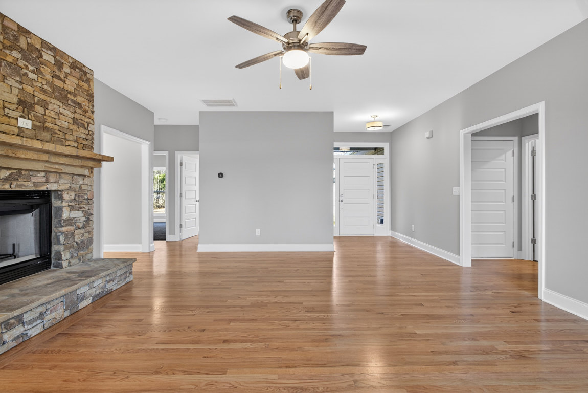 Living room with hardwood floors, white walls, ceiling fan with light, and white doors; fireplace visible on left side