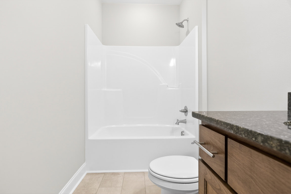 White bathtub with silver fixtures beside a modern toilet, light tile flooring, wall-mounted metal towel bar, and a sleek countertop with chrome tap and shower head.