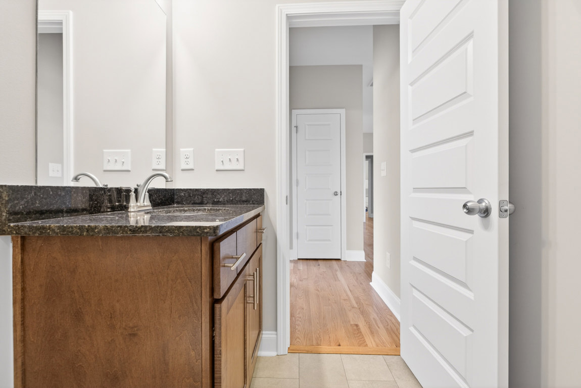 Bathroom with marble countertop vanity, undermount sink, wood flooring, white door with silver knob, and white light switch on wall.