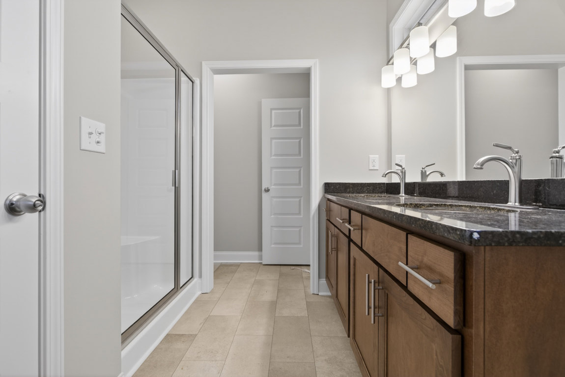 Modern bathroom featuring a tile floor, walk-in shower with glass enclosure, white vanity cabinet with silver faucet, and white door with silver handle