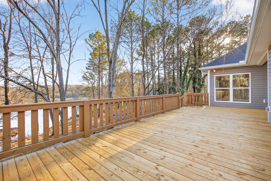 Wooden deck with railing overlooking trees and blue sky, house exterior features large window with a dog inside