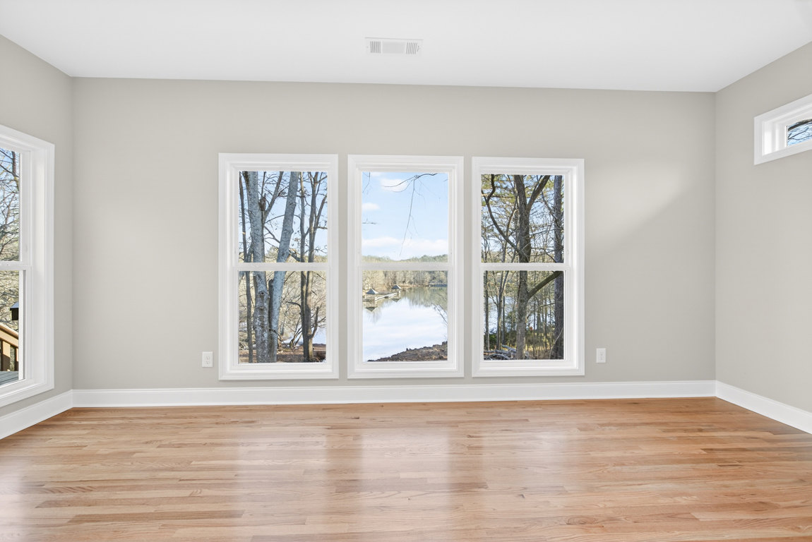 Wood floor with white trim, large window overlooking trees and a river with a dock, white ceiling featuring a vent
