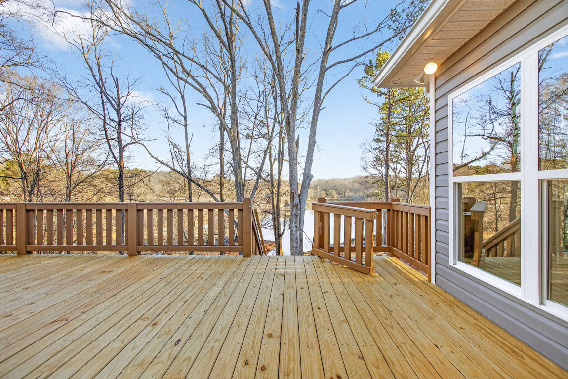 Wooden deck with railing, large window, lake view, and surrounding trees