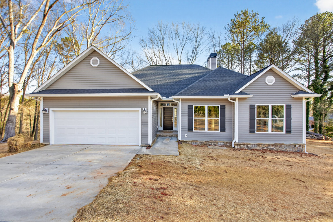 Two-story house with white siding, grey trim, attached garage with white door, concrete driveway, front porch, white-framed windows, and a person visible through one window
