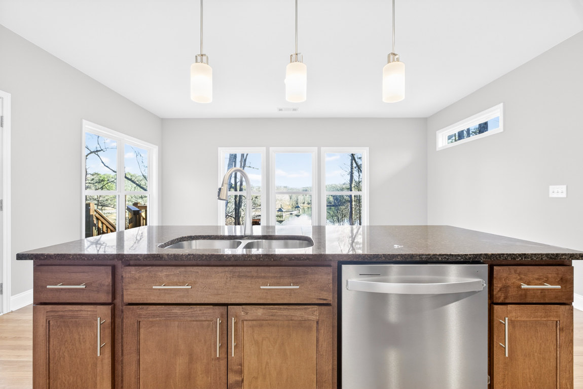White kitchen with shaker cabinets, quartz countertops, stainless steel dishwasher beneath sink, pendant light fixture, large window overlooking trees
