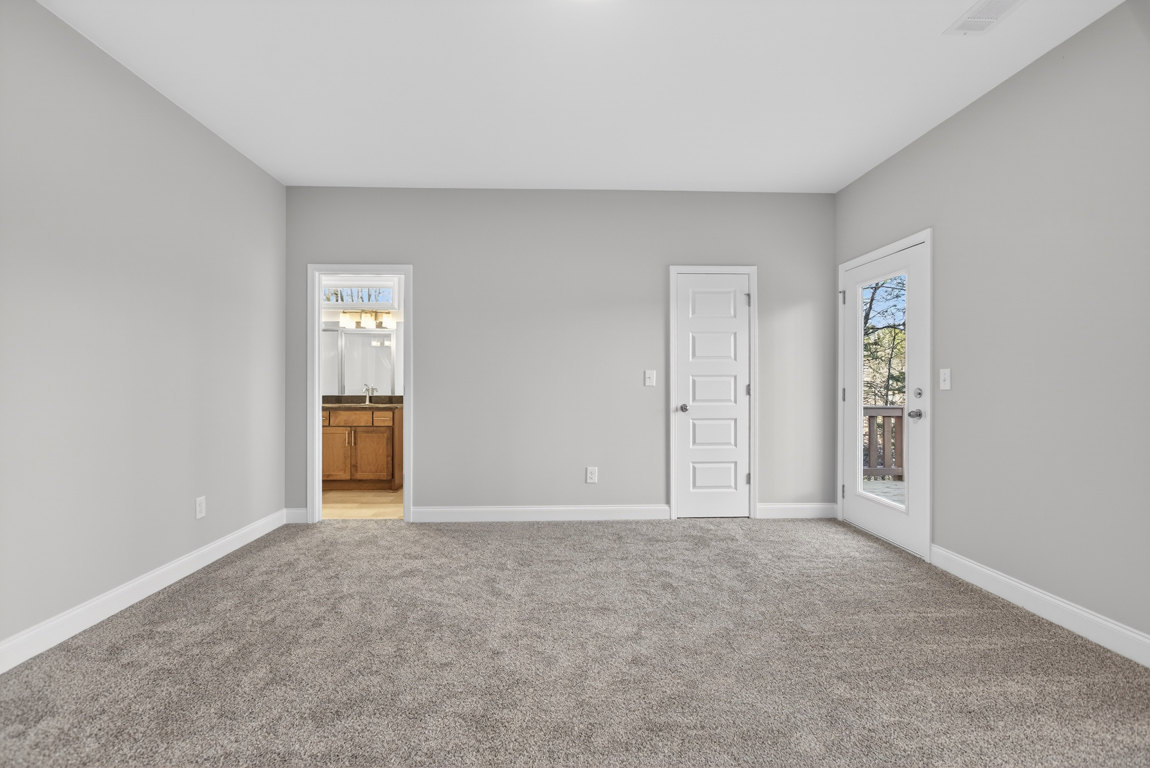 Carpeted room with white paneled door featuring silver knob, glass door opening to deck with metal railing, visible bathroom sink and mirror, close-up of kitchen cabinetry and