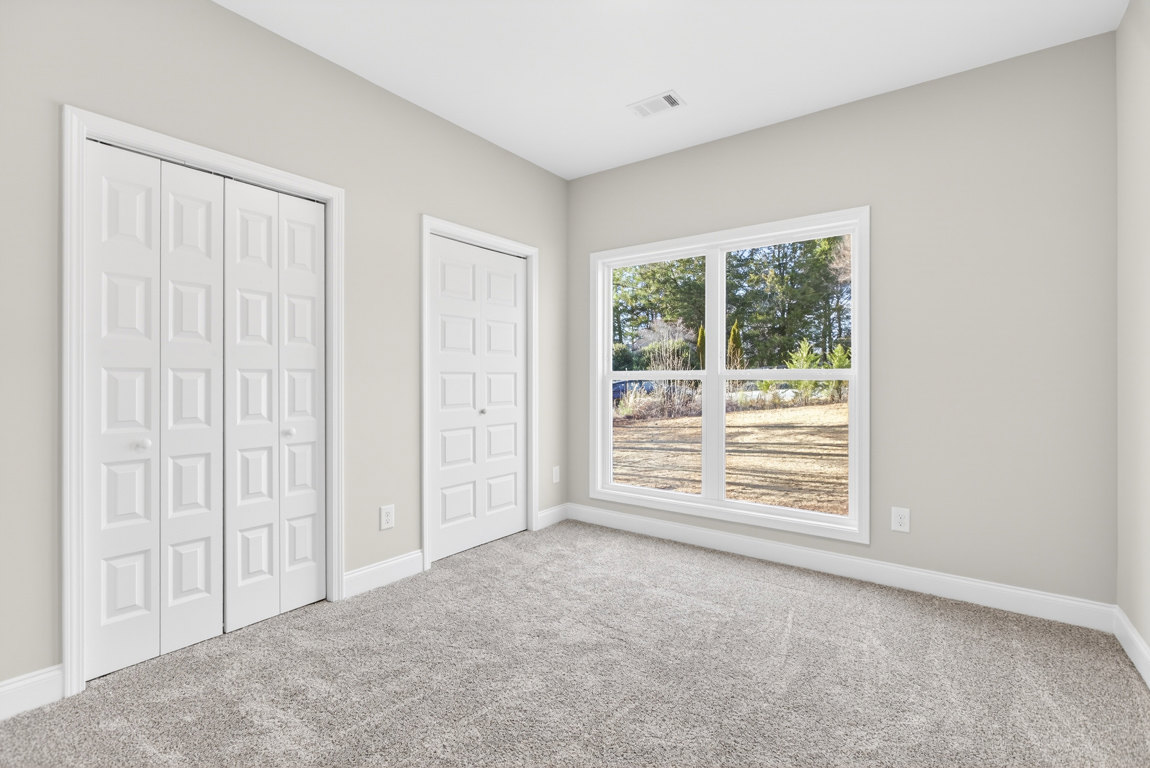Carpeted room with white closet doors featuring square panels, single white door, window showing trees outside, white ceiling with air vent