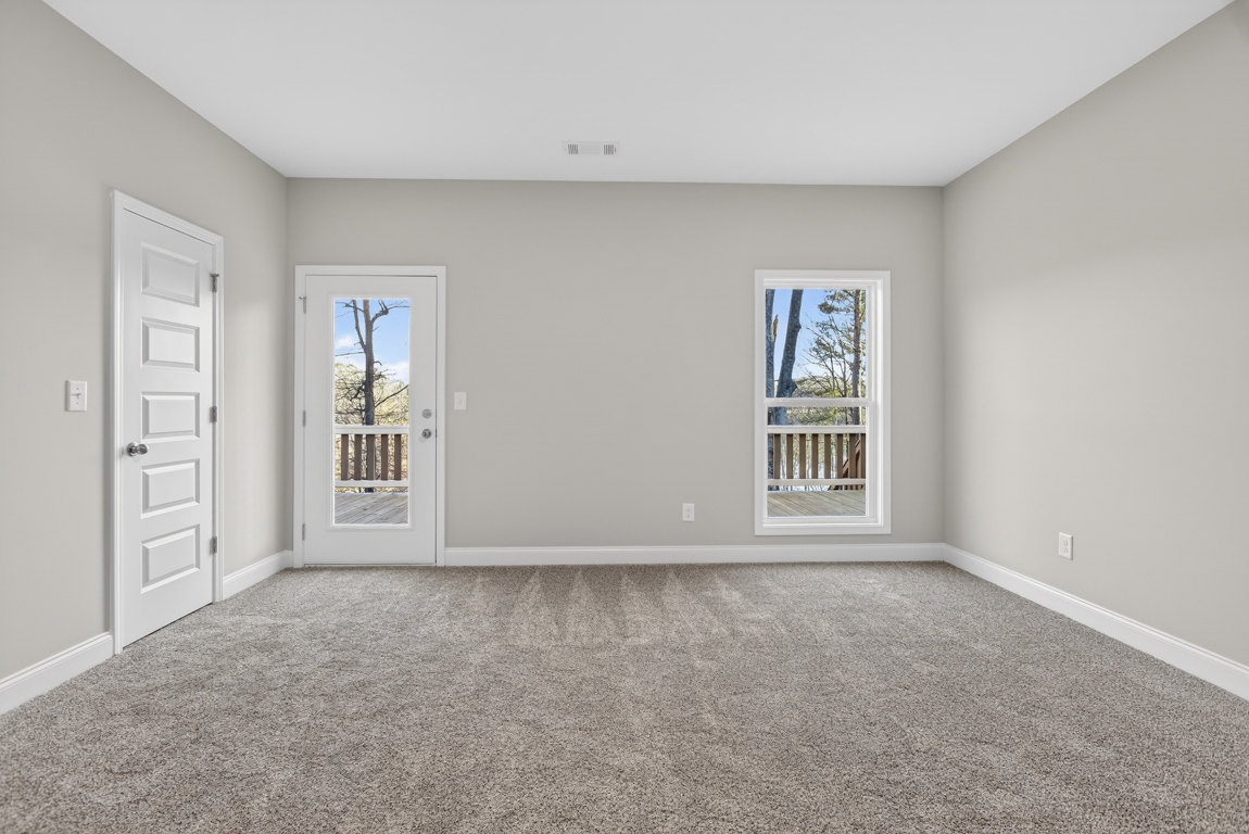 White-walled room with patterned carpet, two white doors—one with a window showing a tree outside—and a deck visible through the glass, window with white trim, person standing near