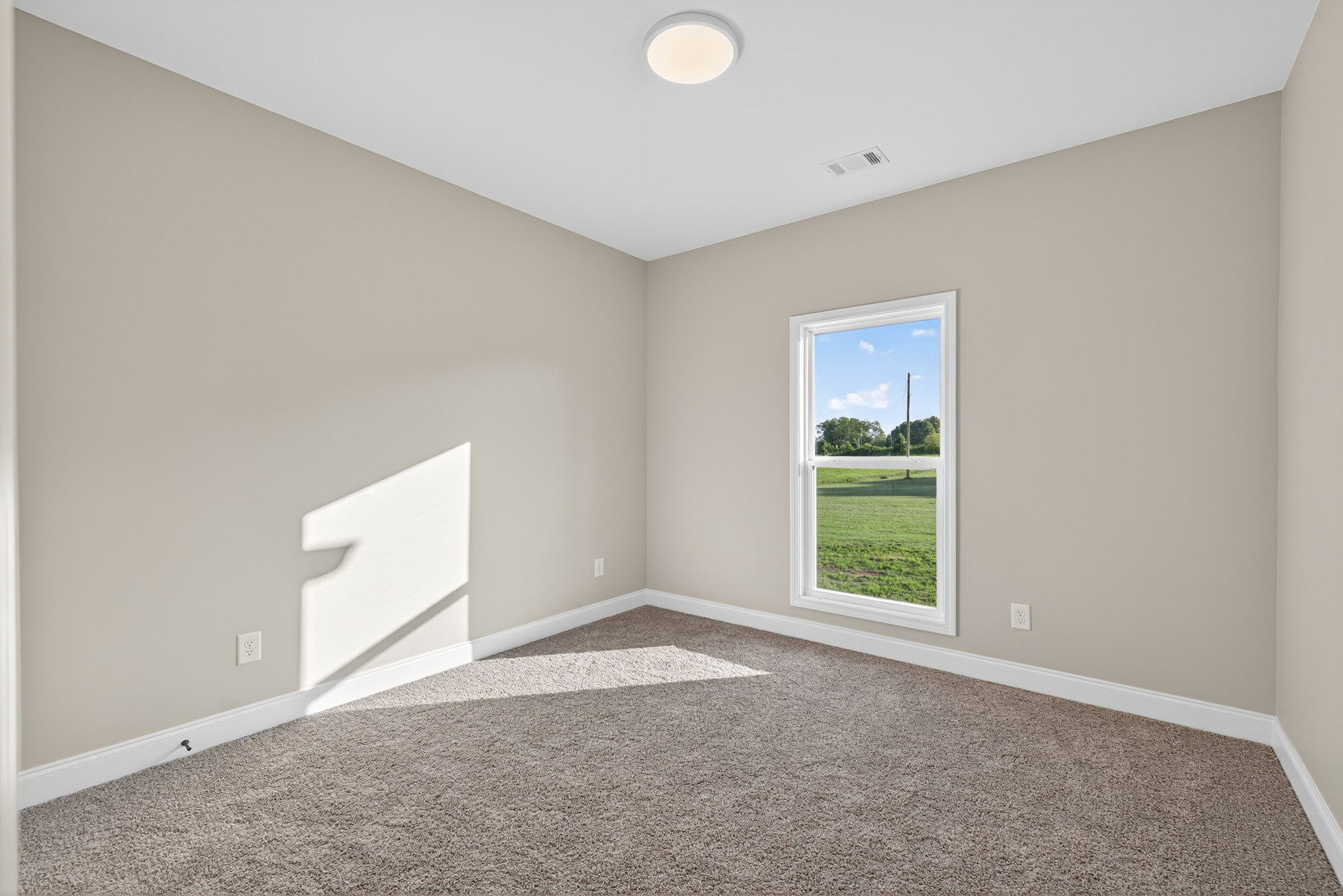 Carpeted room with white walls, large window overlooking grassy yard, sunlight casting shadows on floor and wall