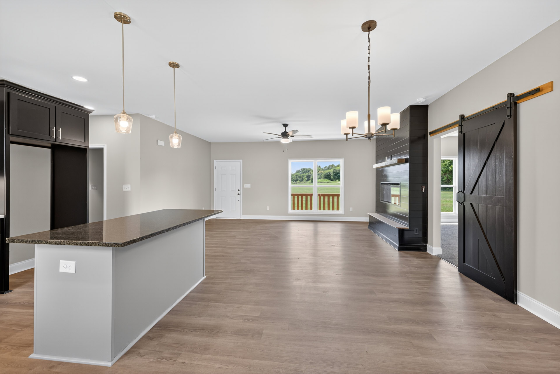Open-concept kitchen with marble countertop, white cabinetry, fireplace, white door with silver doorknob, large window overlooking grassy field, light-colored flooring, and smooth
