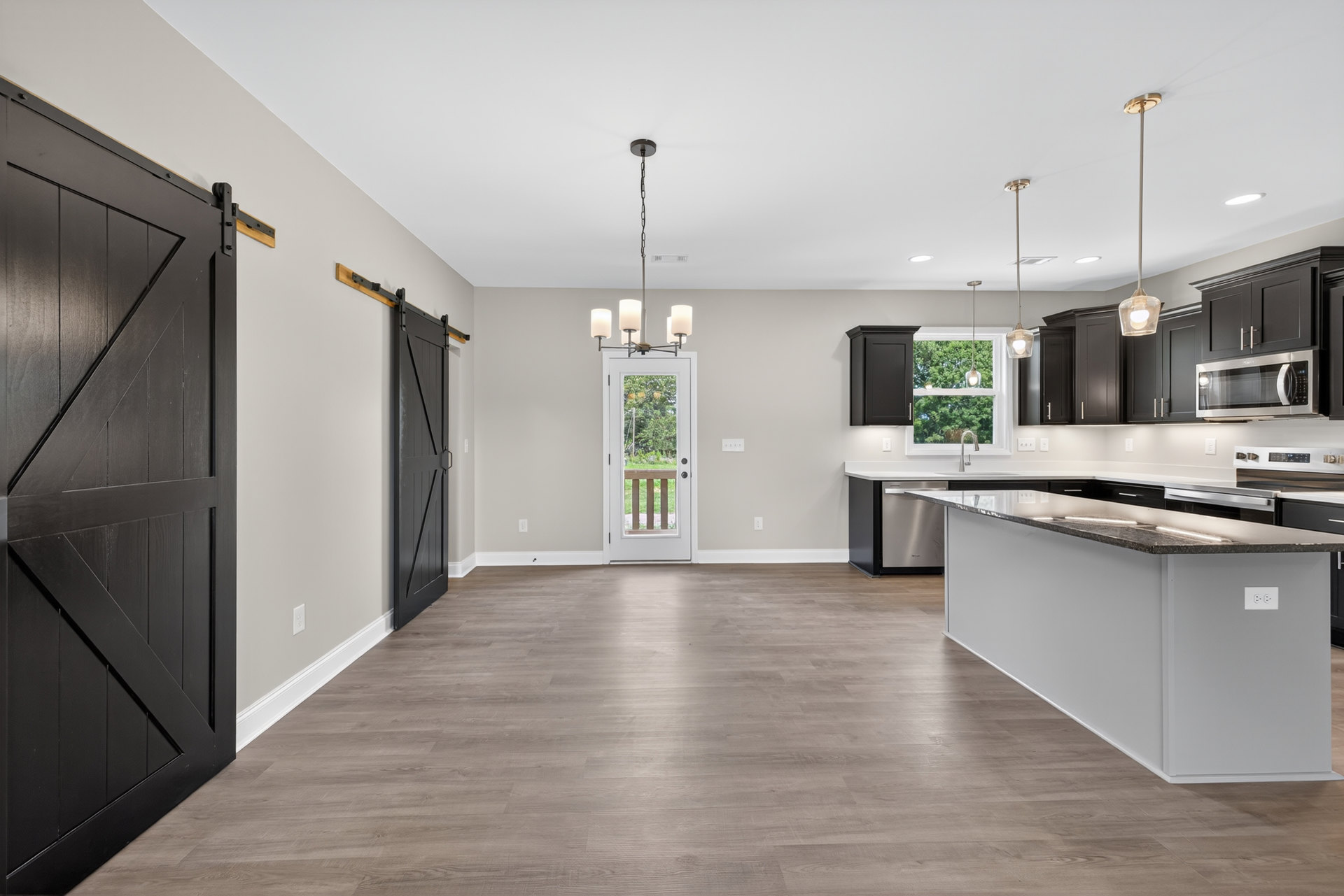 Open kitchen and dining area featuring wood cabinetry, stone countertops, kitchen island with built-in stove, stainless steel appliances, sliding glass doors overlooking trees and