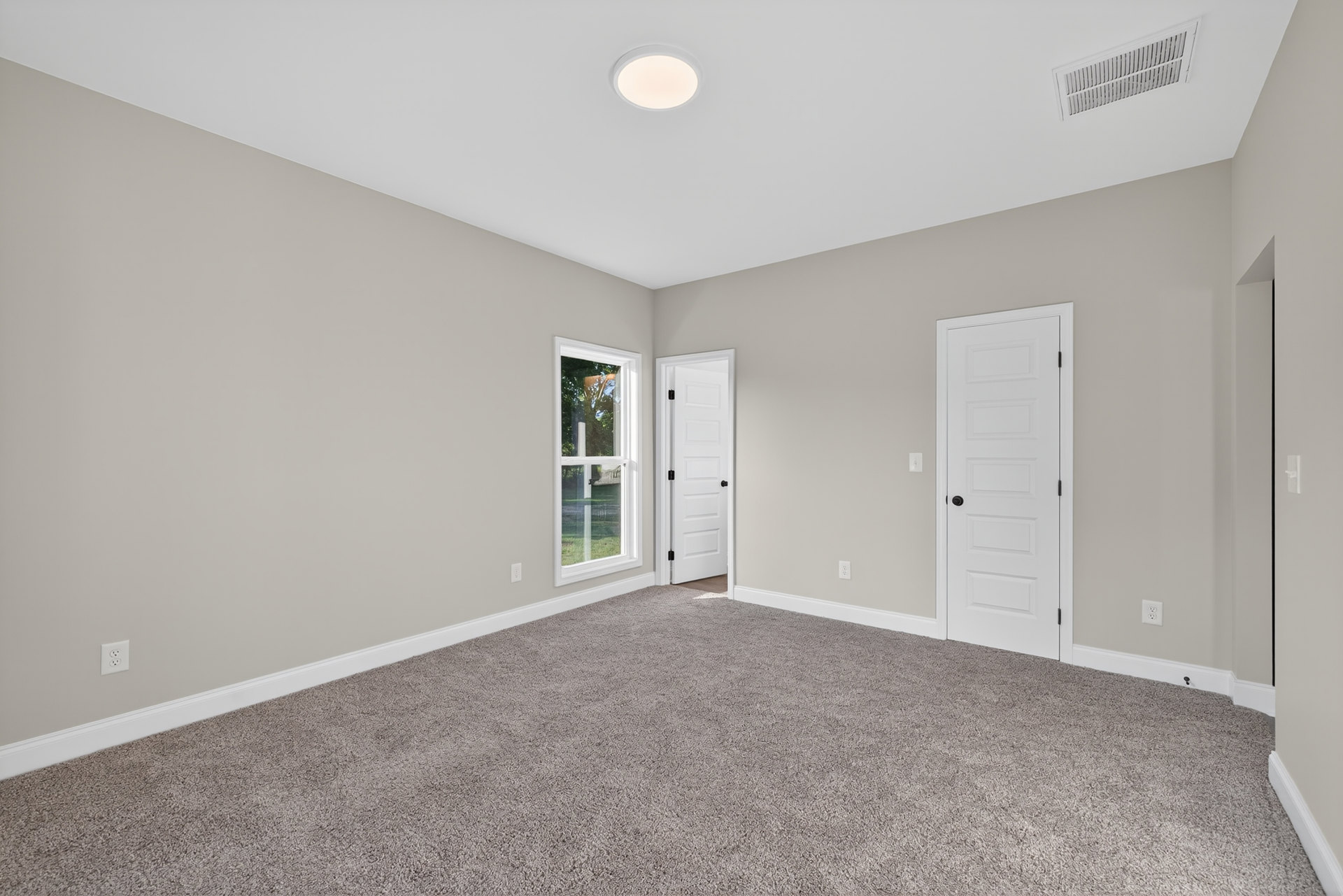 Bedroom with soft beige carpet, white paneled doors featuring black knobs, white-framed window, ceiling vent, and recessed light fixture