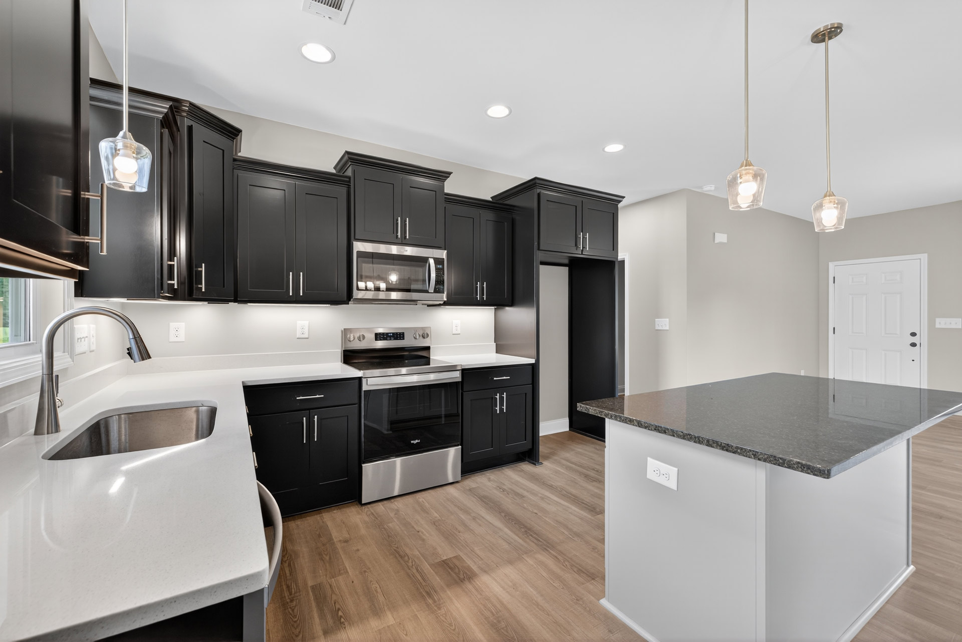 Kitchen with matte black cabinets, wood plank flooring, stainless steel oven and stove, black granite-topped island, built-in microwave, white door with black hardware, and