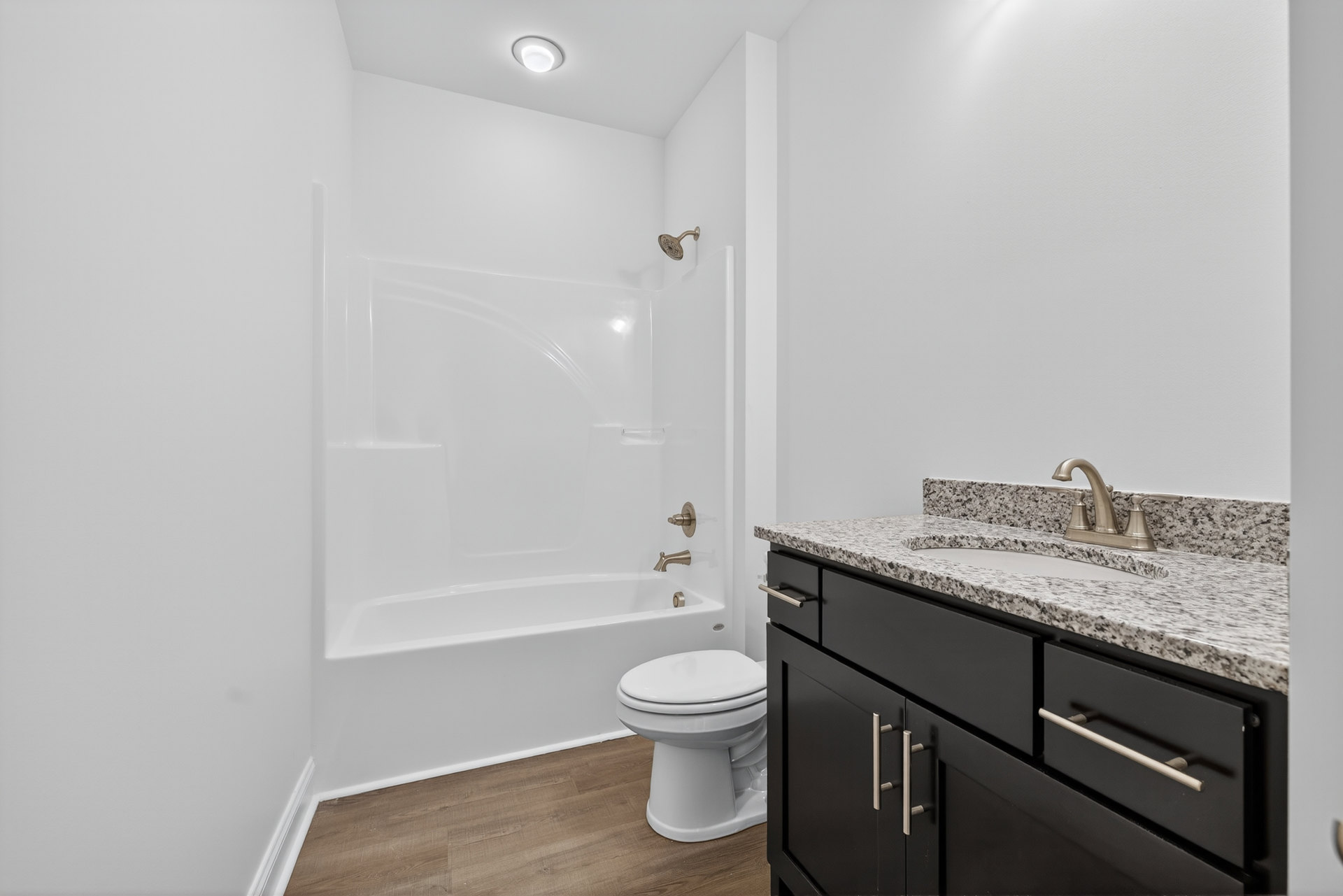 Bathroom with white toilet, rectangular sink set in light-colored countertop, tile flooring, white bathtub, wall-mounted shower head, and white cabinetry with drawers.