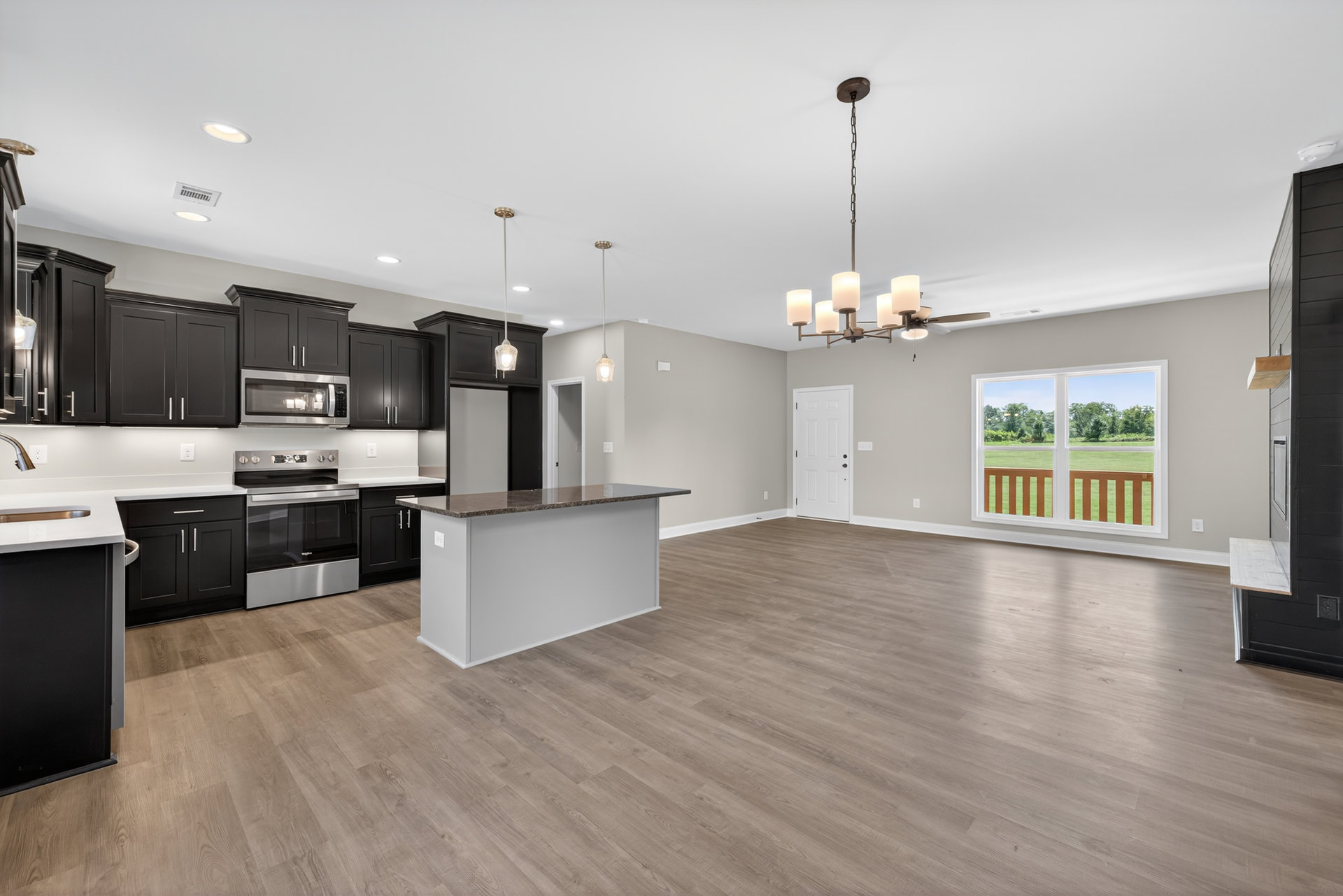 Open-concept kitchen and living room featuring wood flooring, white cabinetry, stone countertops, stainless steel appliances, large windows overlooking grassy yard and trees