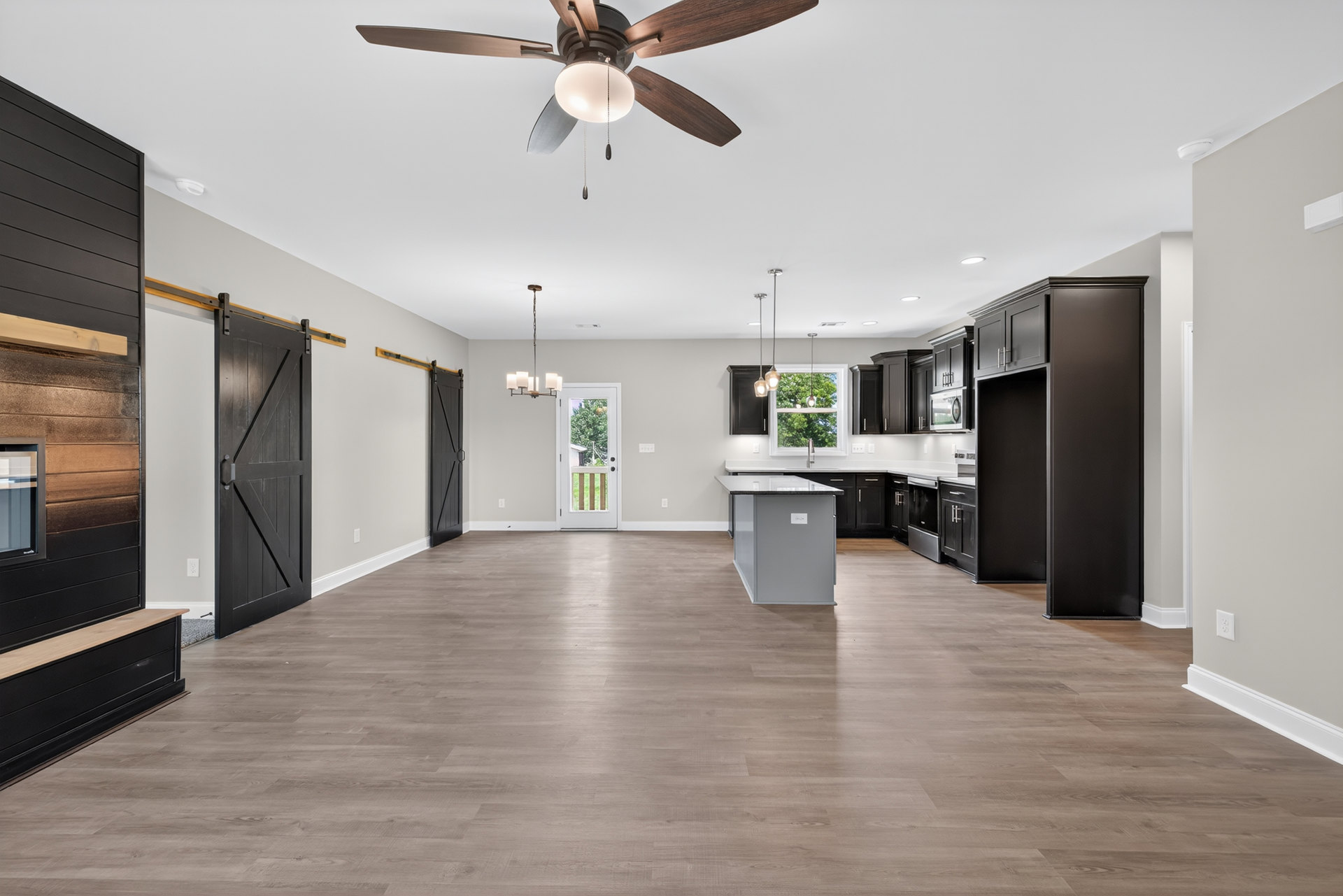 Open-concept kitchen with a central island, wood laminate flooring, white cabinetry, ceiling fan with light fixture, and neutral walls