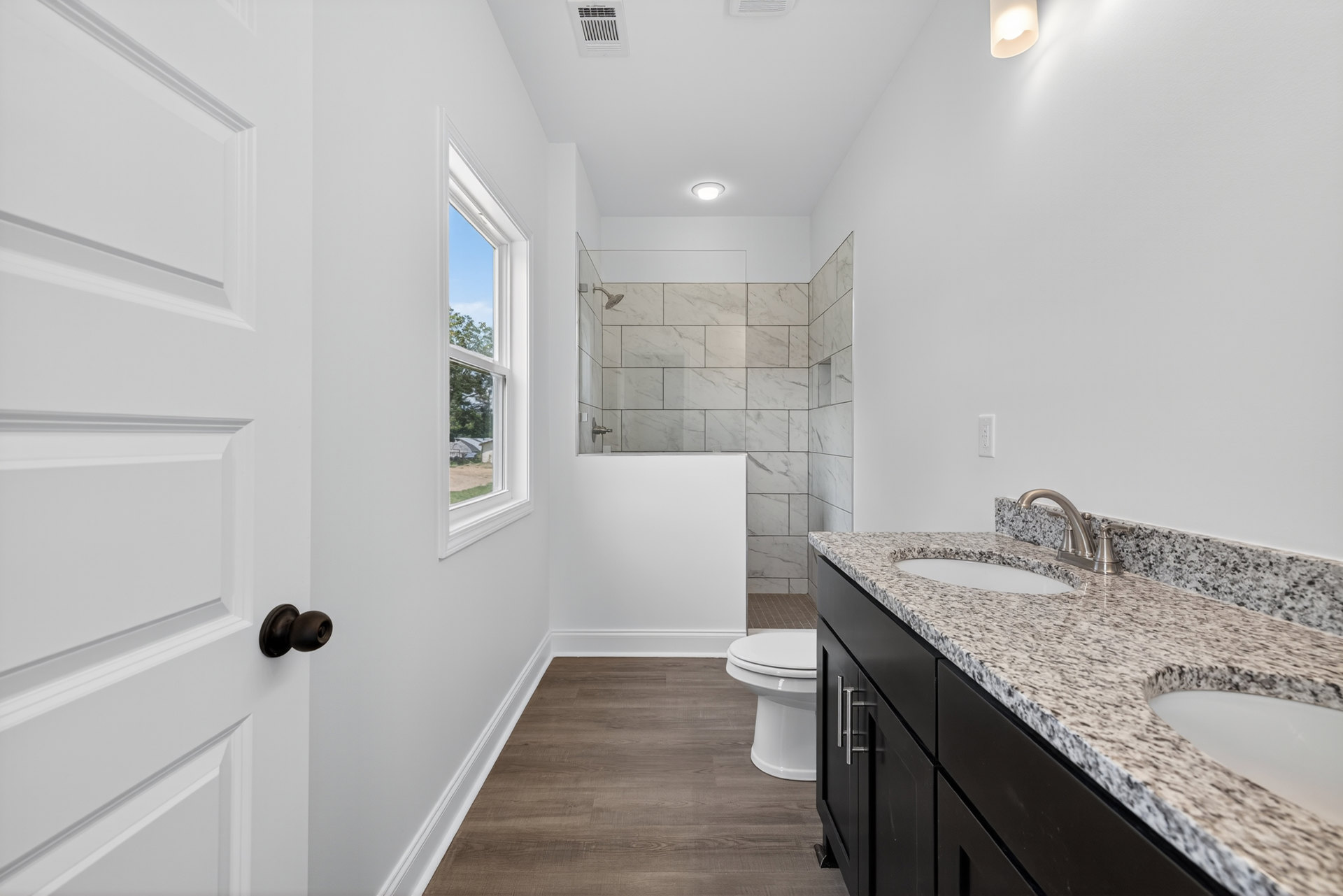 Bathroom featuring marble countertop vanity, glass-enclosed tile shower, white toilet, brushed metal faucet, and light wood flooring