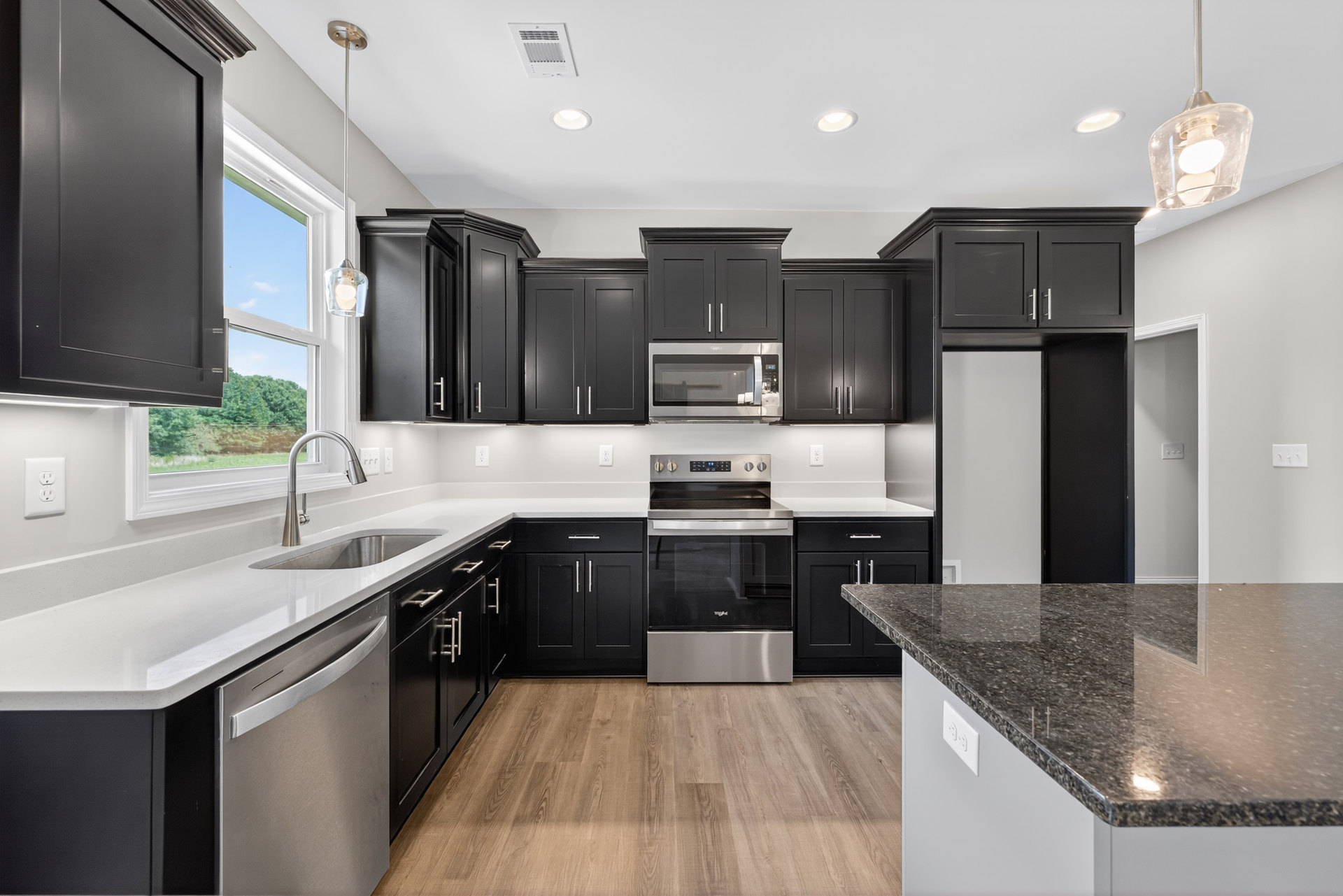Black kitchen cabinets with silver hardware, white granite countertop, stainless steel oven, built-in white microwave with glass door, tile backsplash, modern light fixture