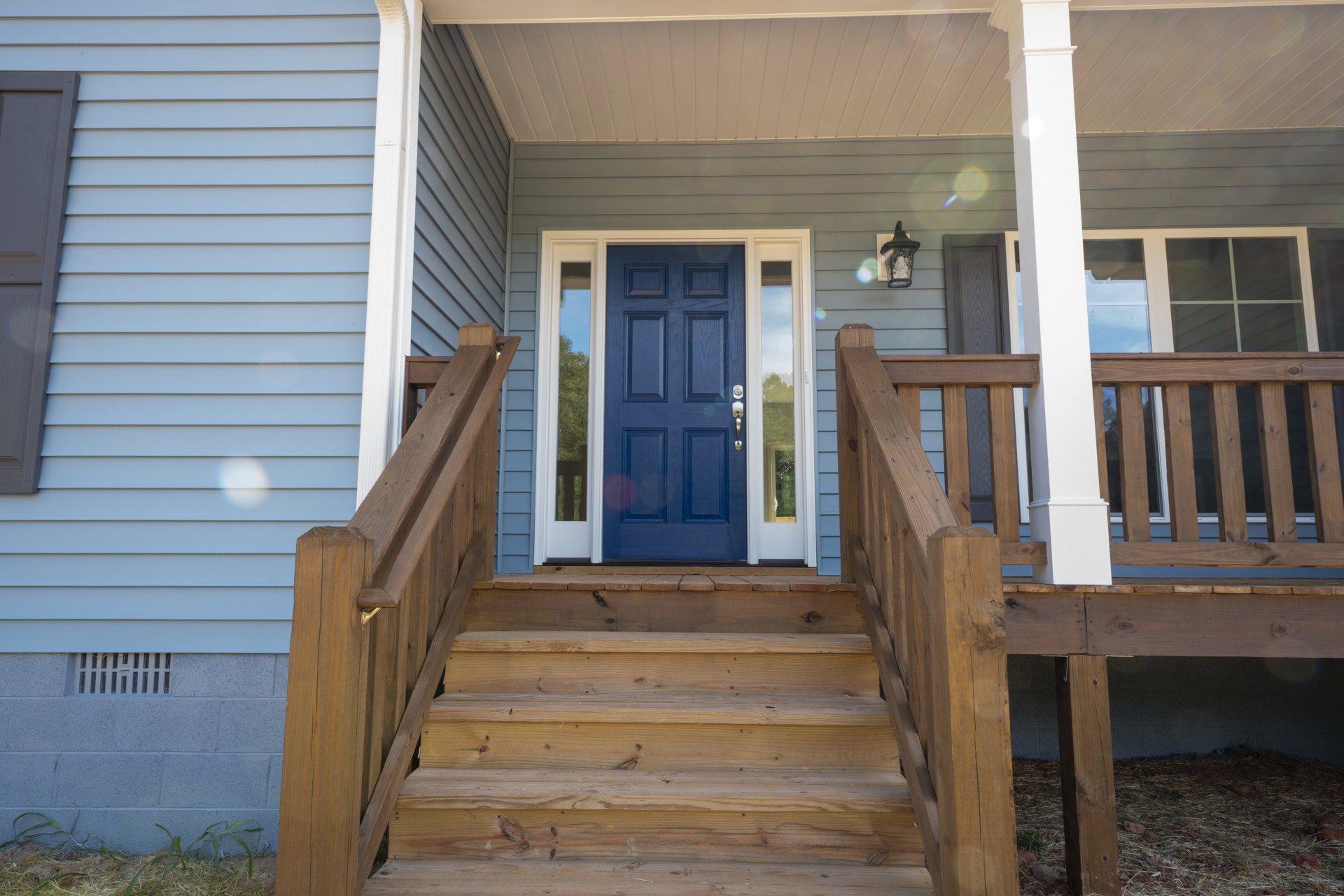 Blue front door with glass panes, wooden stairs, white siding, porch deck, and window.