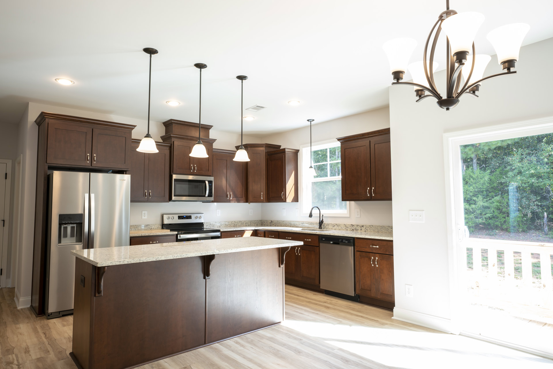 Spacious kitchen featuring a large central island with stone countertop, stainless steel refrigerator with ice and water dispenser, built-in microwave in wood cabinetry, silver