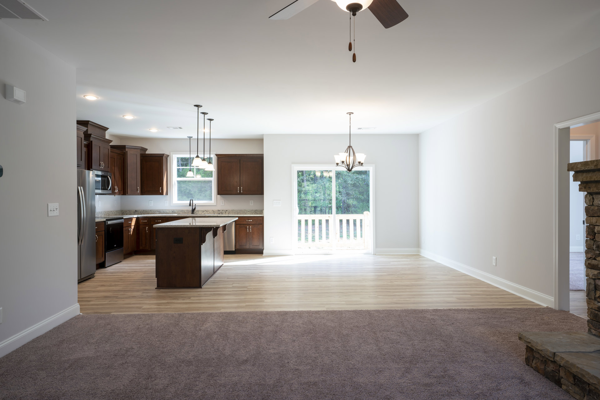 Open-concept kitchen and living room featuring a ceiling fan, granite kitchen island, black refrigerator with silver handle, light fixture, laminate flooring, and carpeted area.