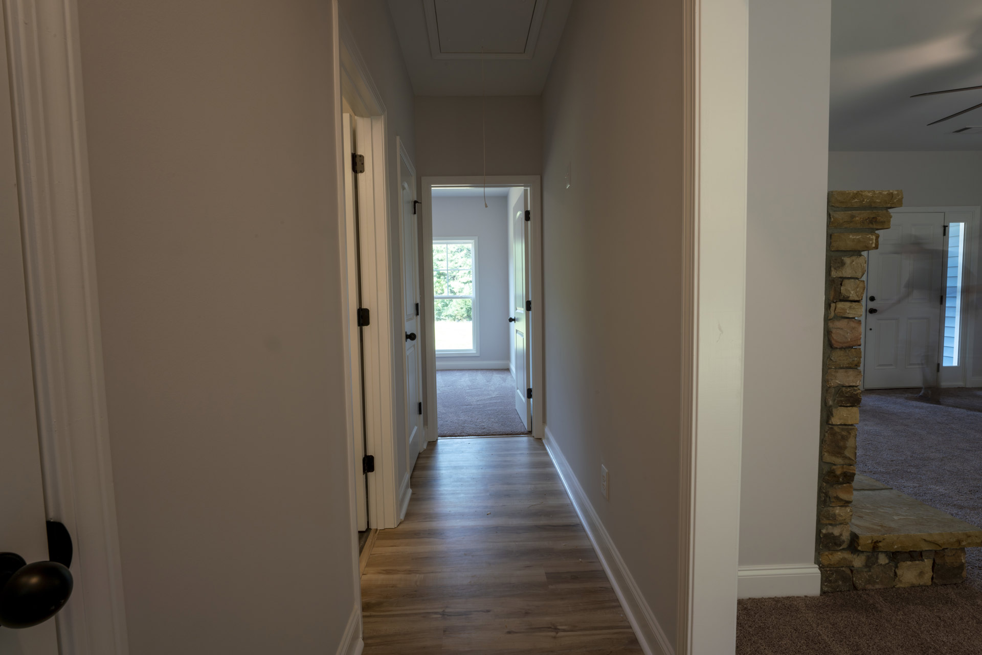 Hallway with white plaster walls, hardwood flooring, open door leading to a window with trees visible outside