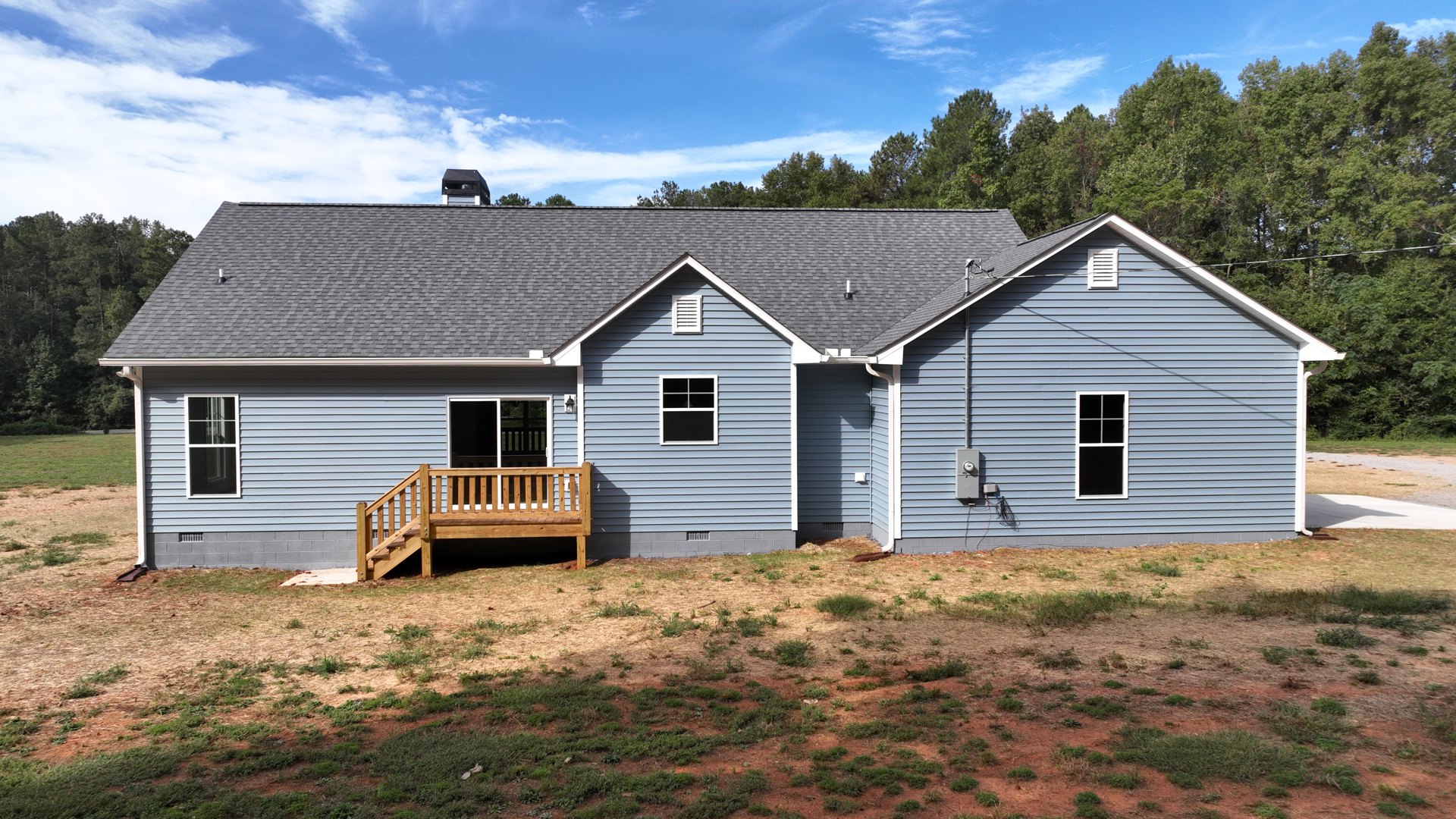 Two-story house with white siding, covered front porch, wood deck with stairs, black-trimmed windows, and grassy lawn