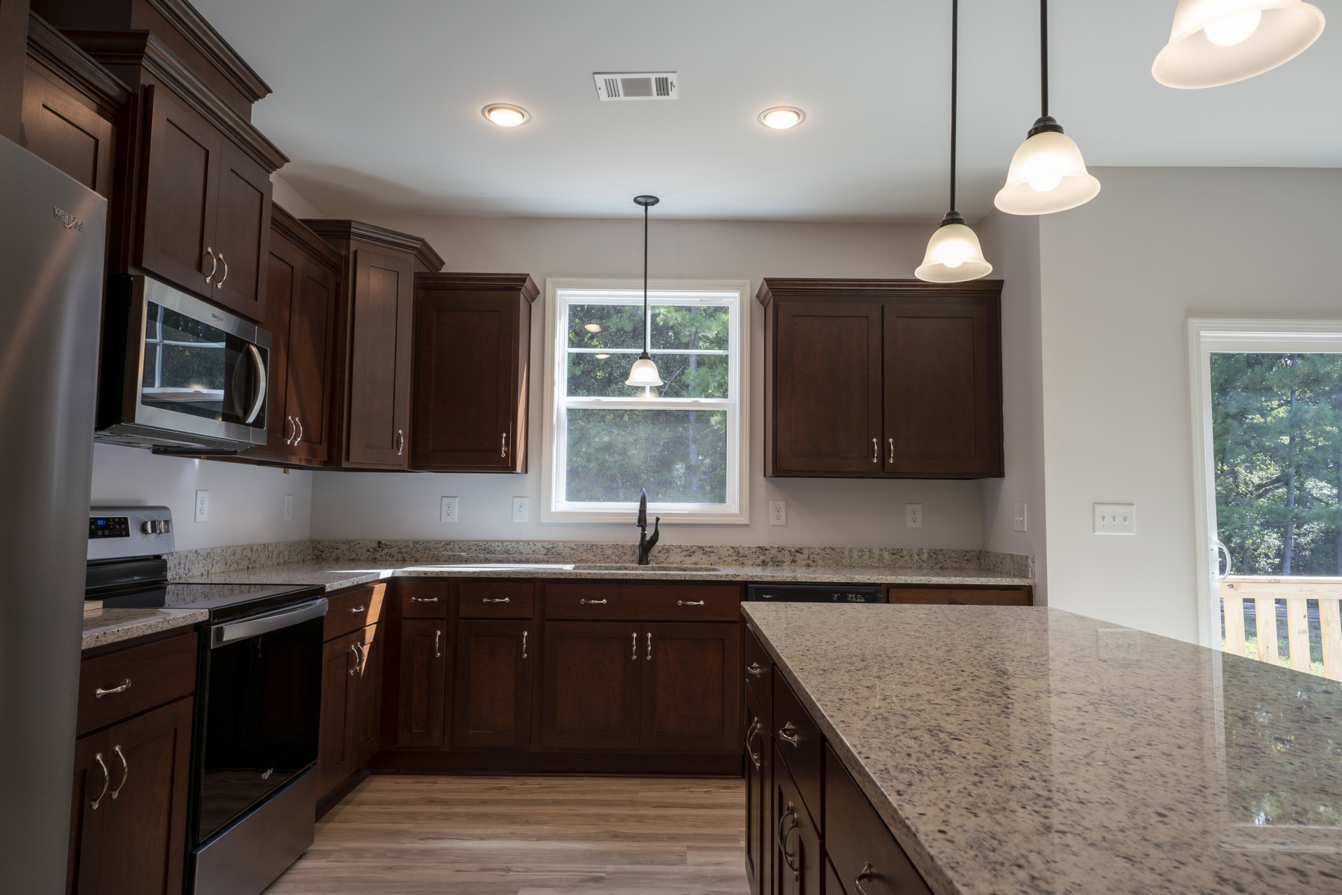 Dark wood kitchen cabinets with silver handles, white granite countertop, stainless steel microwave, ceiling light fixture, and built-in sink.