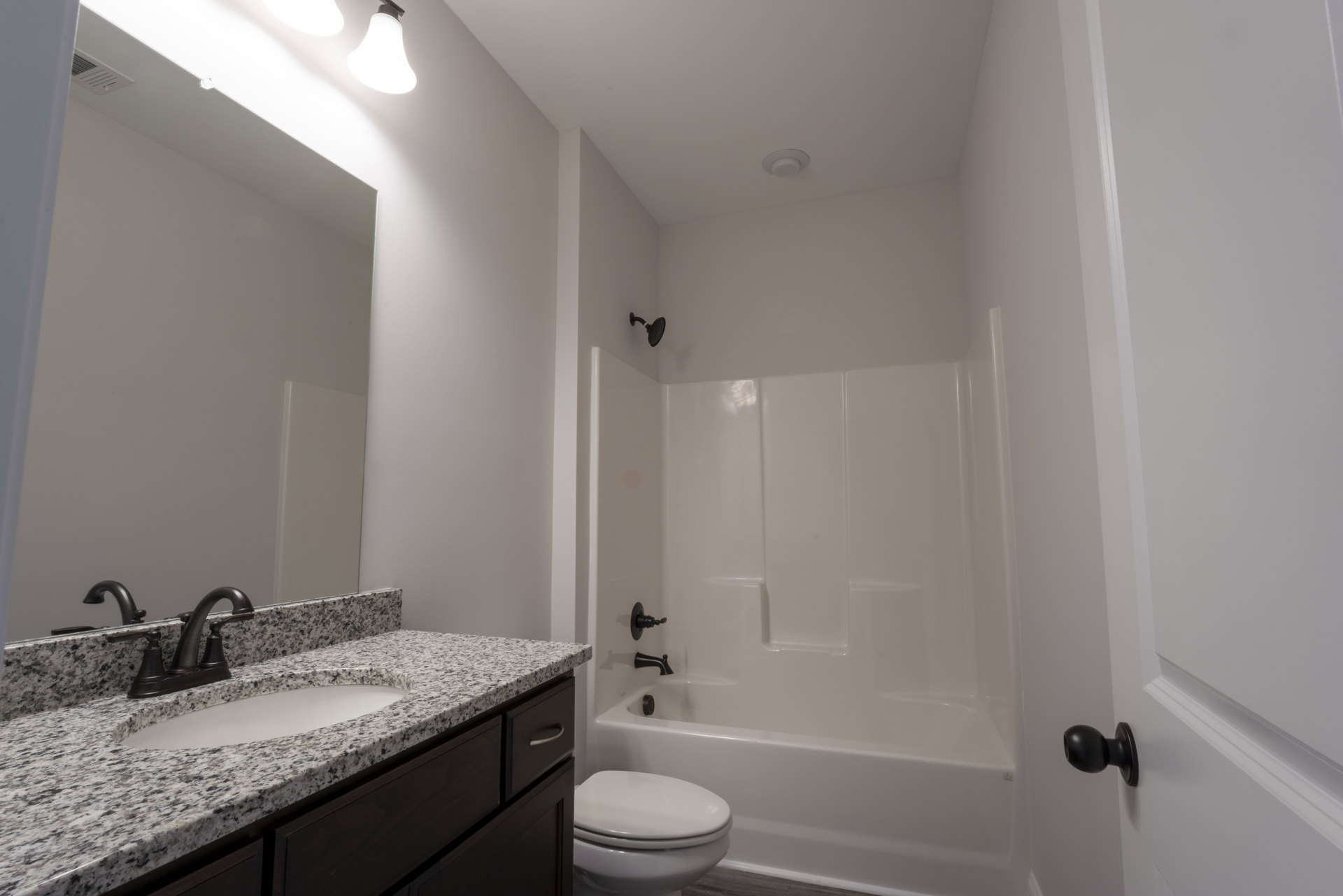 White bathroom with rectangular sink and chrome faucet on light countertop, modern toilet with closed lid, black door knob on white wall, neutral tile flooring
