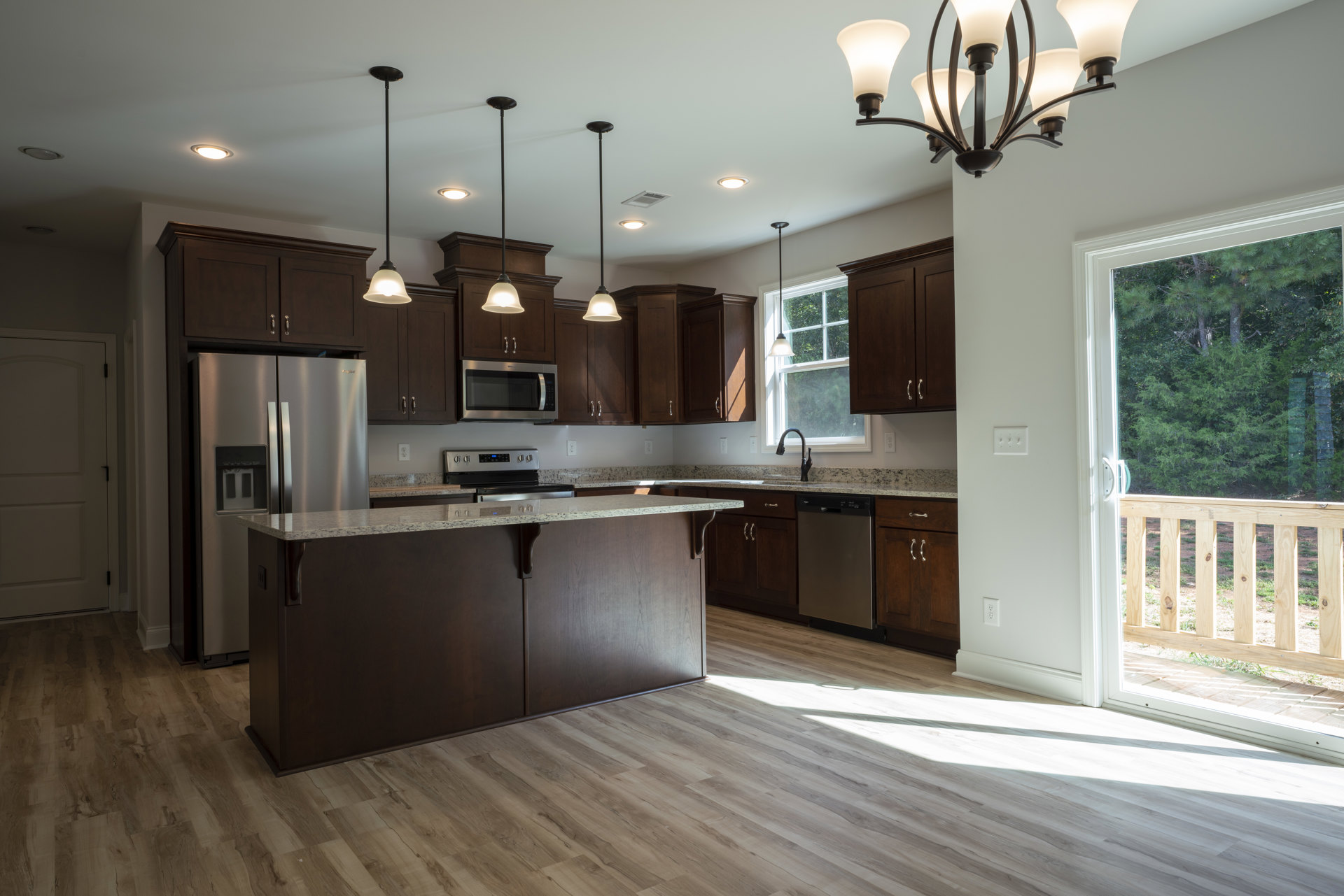 Modern kitchen featuring a central island with white quartz countertop, stainless steel refrigerator, built-in microwave with black handle, light wood cabinetry, undermount sink