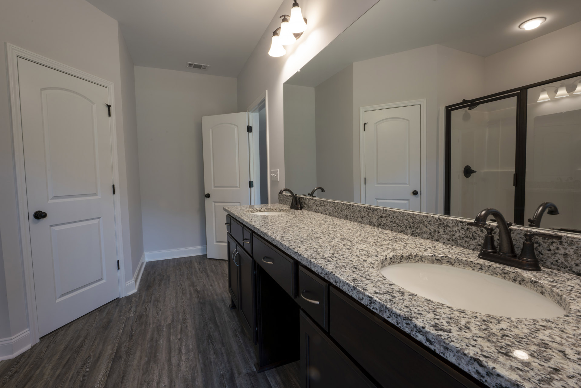 Bathroom with double vanity featuring undermount sinks, quartz countertop, large framed mirror, white cabinetry, black hardware, and three-light fixture above sinks