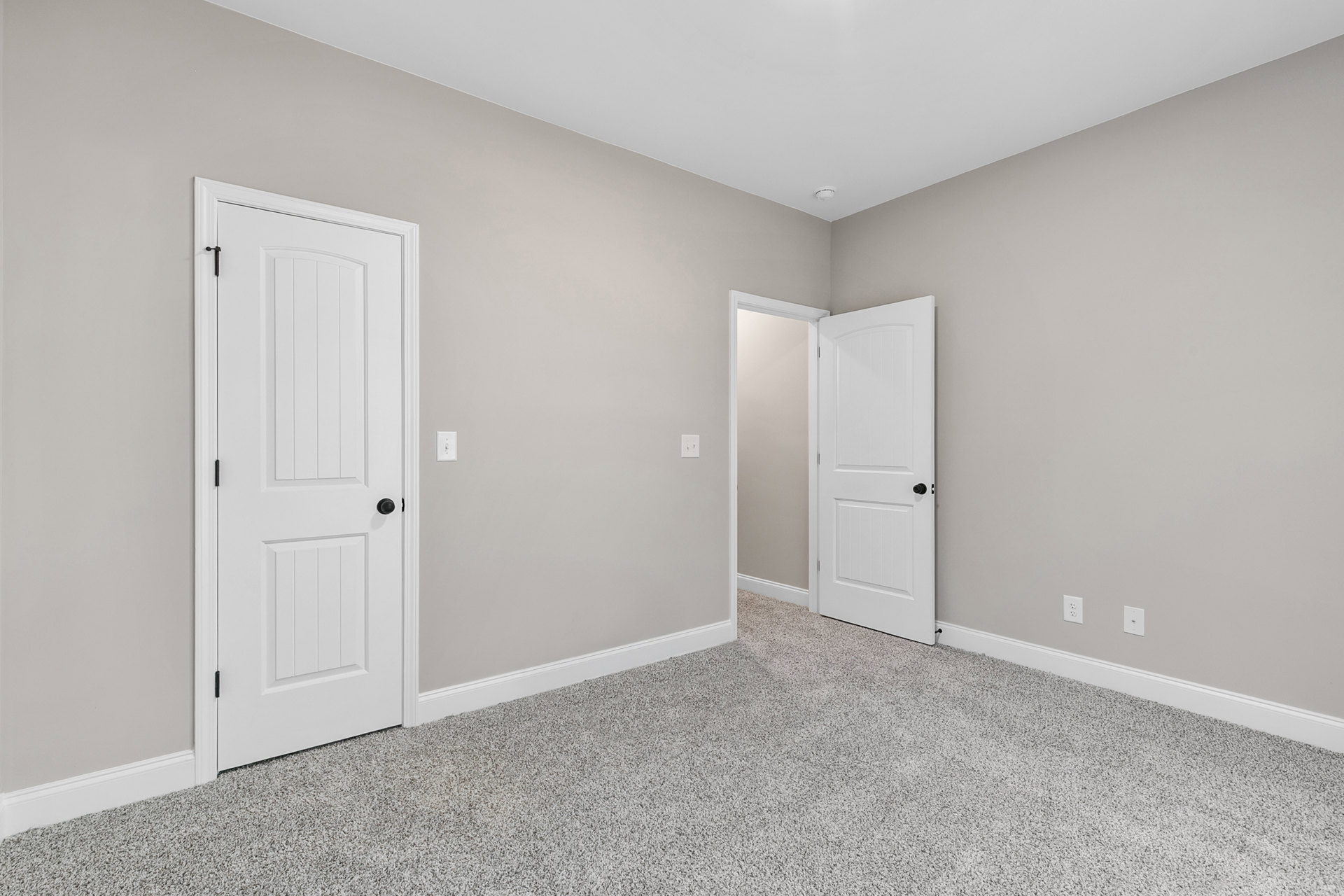 Carpeted room with two white doors featuring black knobs, white trim along the floor, and smooth plaster walls.