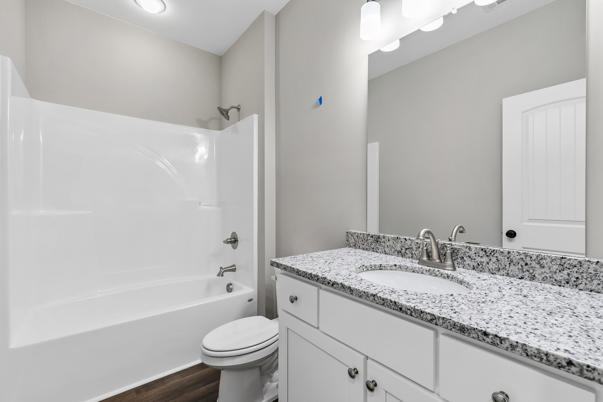 Bathroom with white bathtub, closed white toilet, white paneled door, black and white hardware, tile flooring, and sink set in light countertop