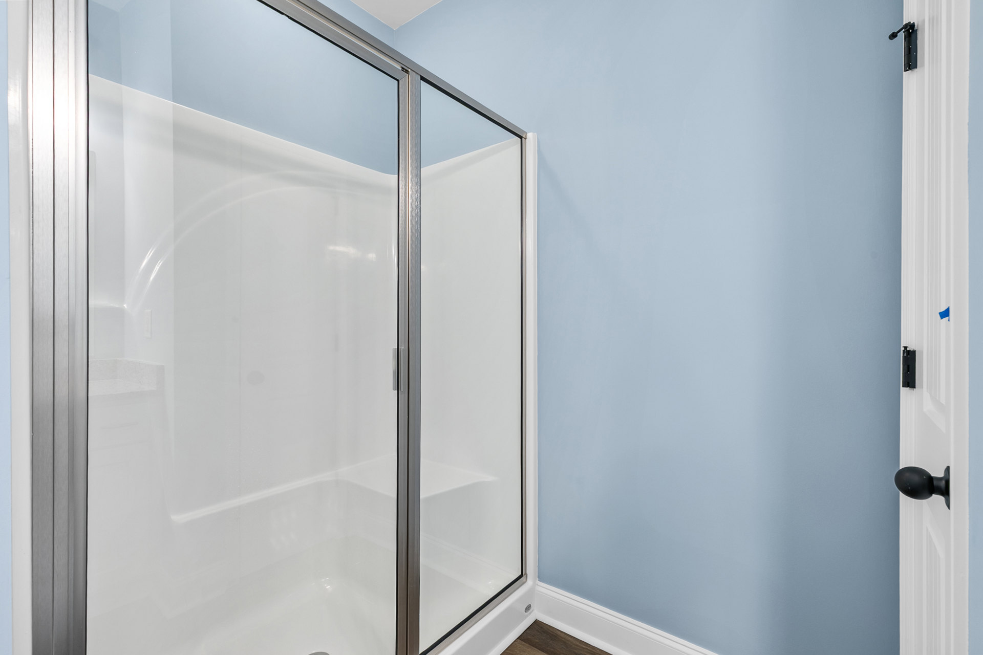 Walk-in shower with clear glass doors, chrome fixtures, white tile walls, and dark floor tiles