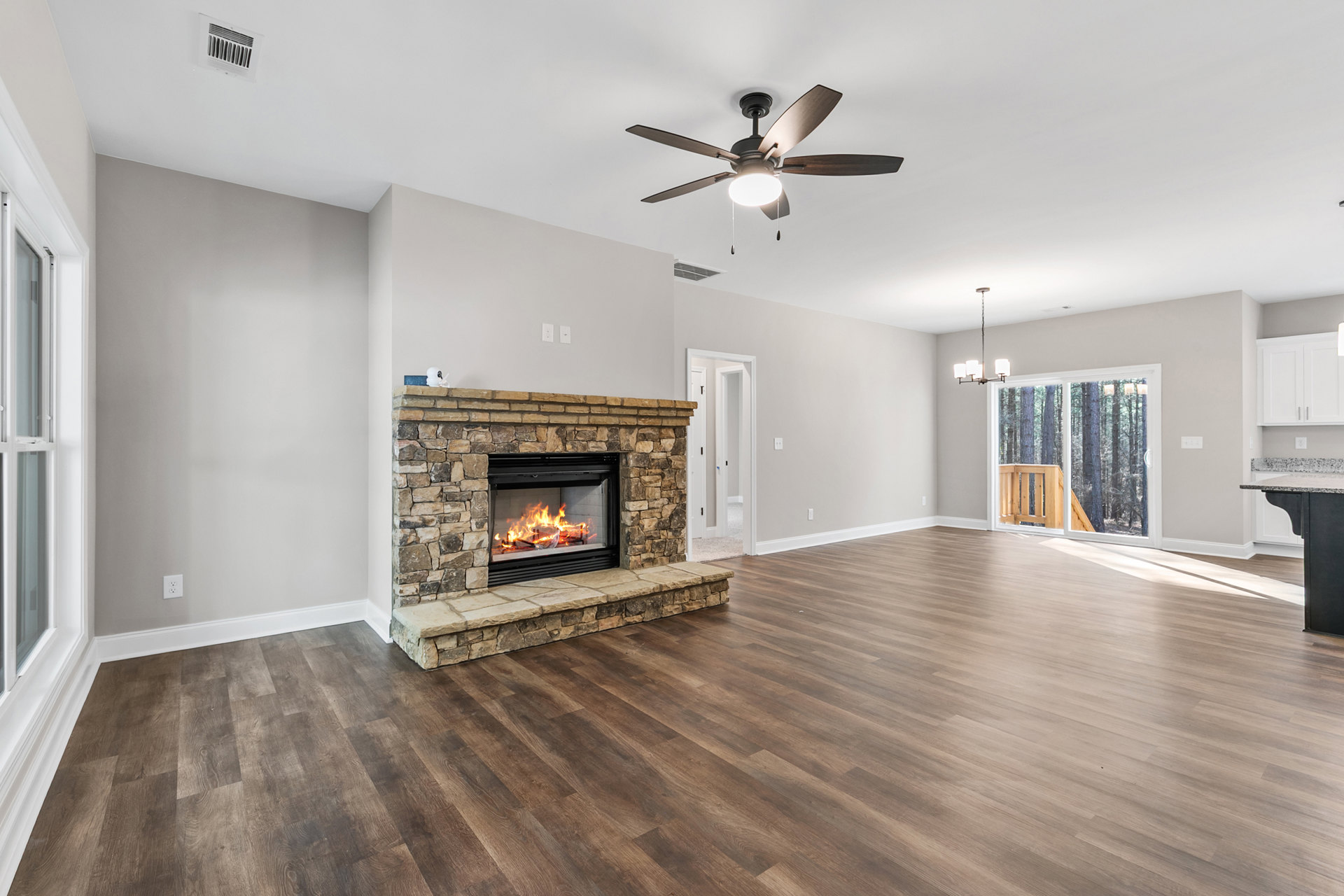 Living room with wood flooring, stone fireplace burning logs, ceiling fan with light, neutral walls, and white trim