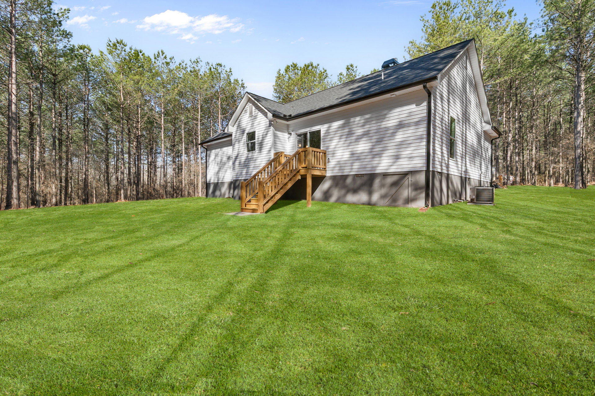 Two-story home with gray siding, wooden porch and staircase, surrounded by green lawn and mature trees