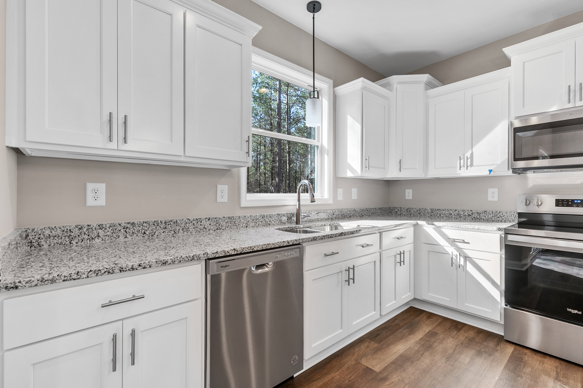 White kitchen cabinets with granite countertops, stainless steel dishwasher, built-in microwave, black oven, electrical outlet on backsplash, window with white frame, and white