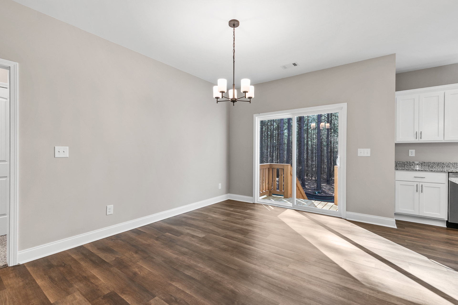 Wood flooring in a bright room featuring a white cabinet, open door, sliding glass door leading to a deck with trees, white light switch on the wall, and a modern chandelier