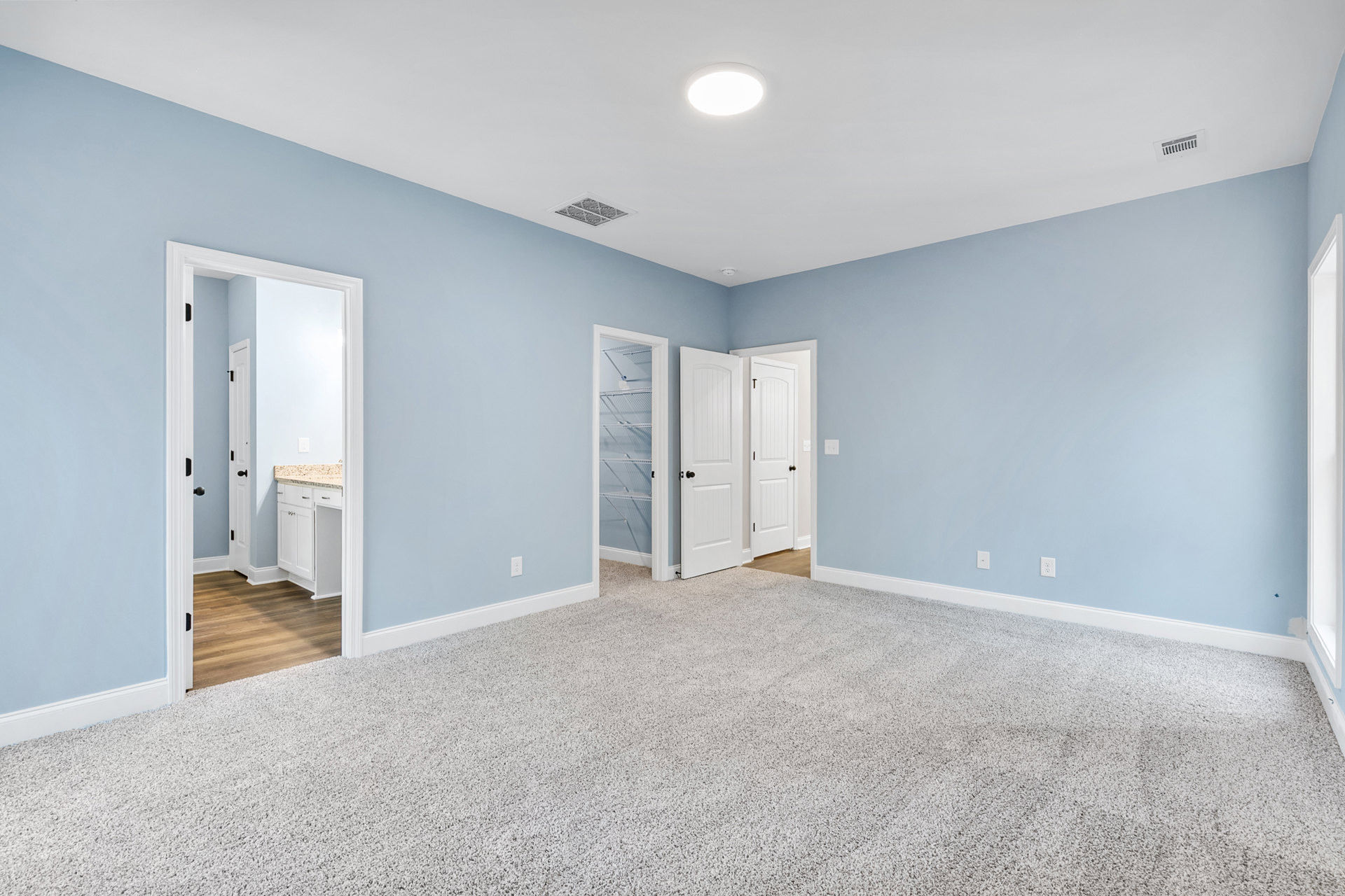 Blue accent walls and white carpeted floor in a room with a white cabinet and shelf, white door with black knob, ceiling vent, and recessed light fixture