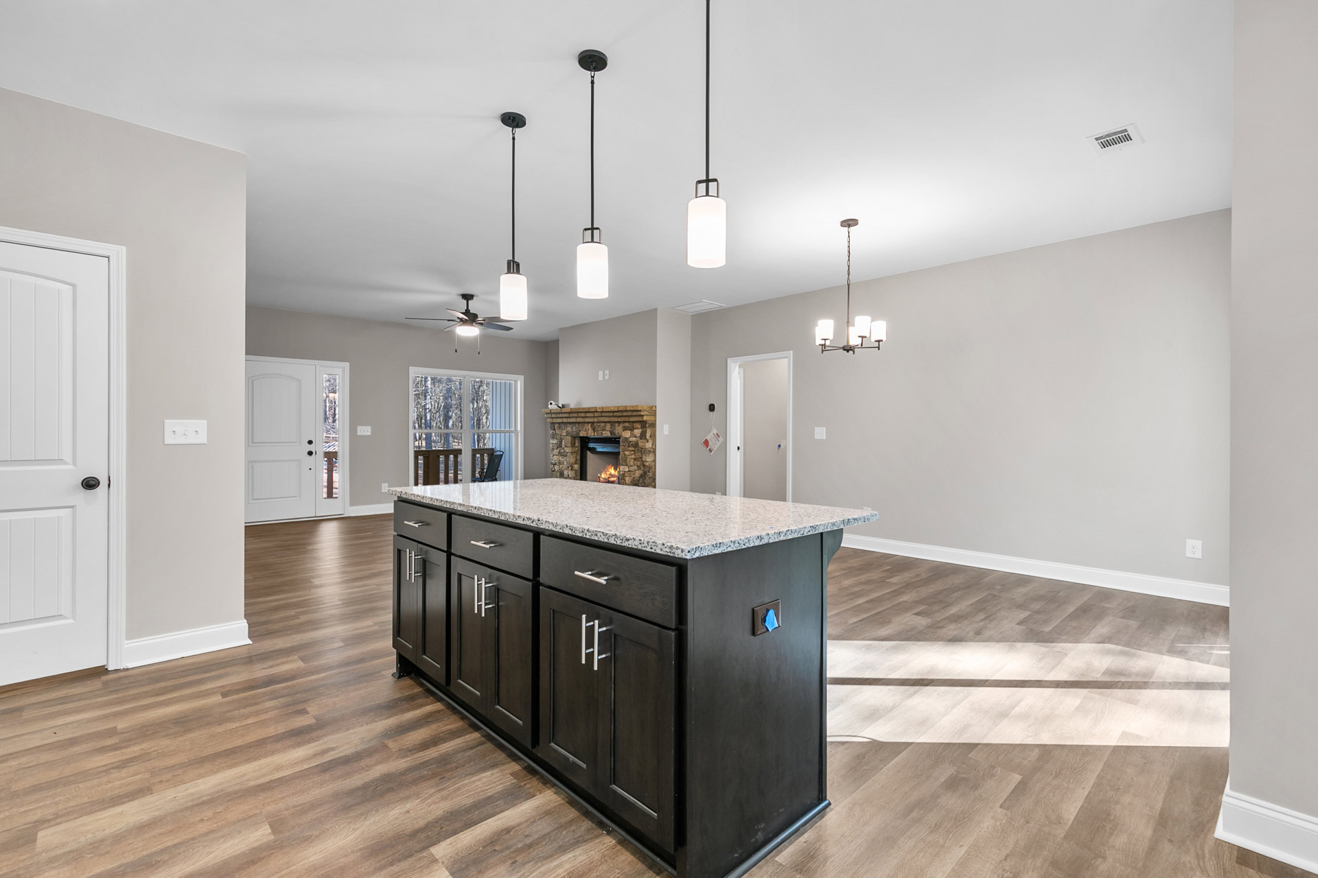Granite kitchen island with built-in sink, white cabinetry, stainless steel appliances, hardwood flooring, fireplace with burning fire, recessed lighting, and nearby window with