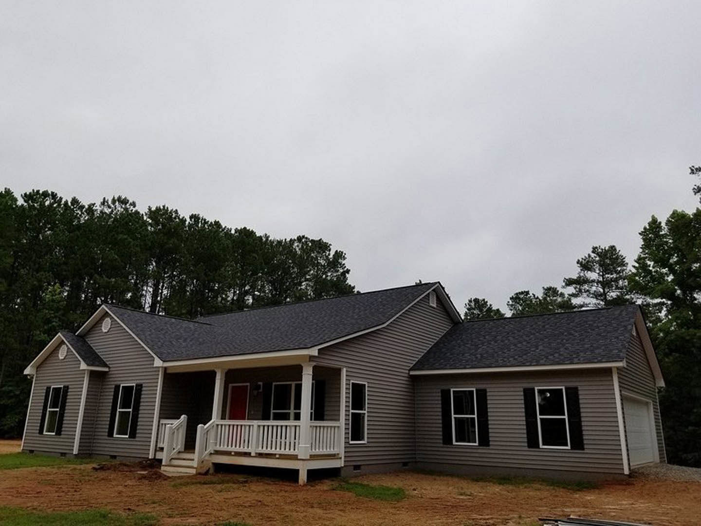 Two-story house with gray siding, white trim, and a covered front porch featuring white railings; large windows with white frames; gabled roof; patch of green grass and small trees