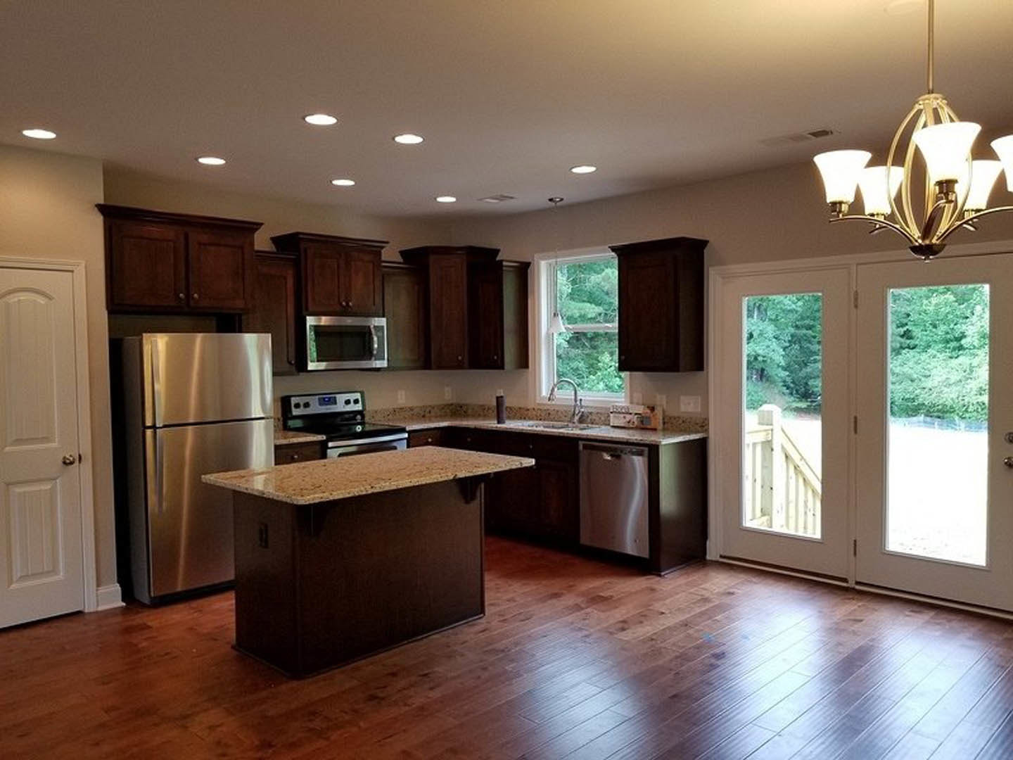 Kitchen with wooden plank flooring, marble-topped island, stainless steel refrigerator, built-in microwave, white cabinetry, glass chandelier, and paneled door