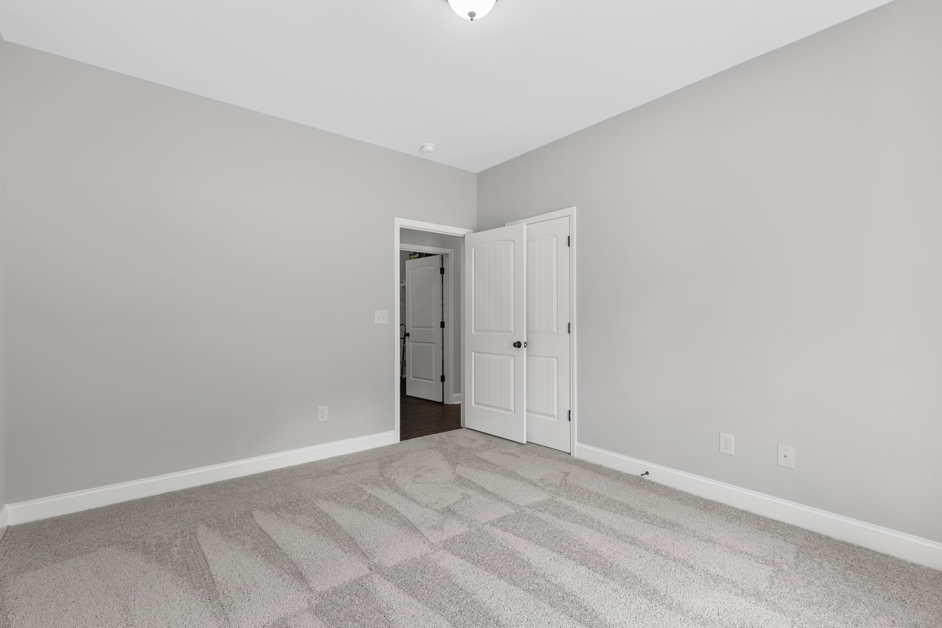 White paneled door with black hardware open to a carpeted room, white walls and baseboards visible