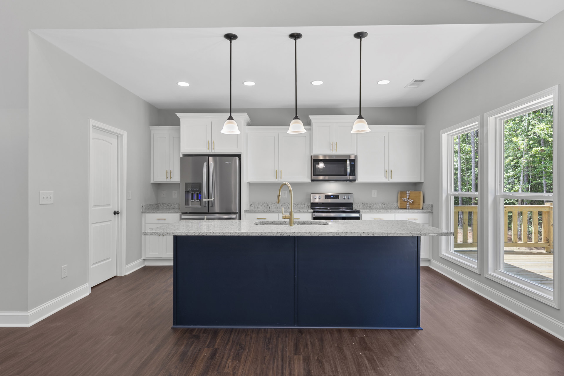 Spacious kitchen featuring a large central island with stone countertop, stainless steel refrigerator, built-in oven and microwave, modern cabinetry, undermount sink, and pendant