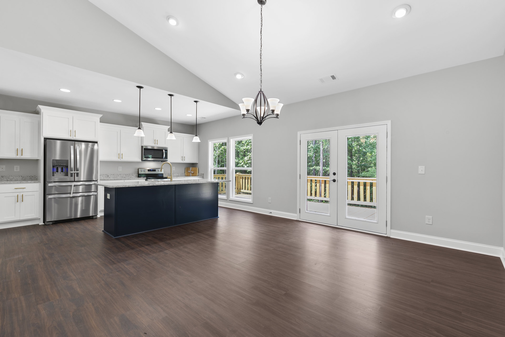 Open kitchen and dining area featuring wood flooring, blue accent wall with windows, stainless steel refrigerator, kitchen counter with sink and mounted TV, glass-paneled double