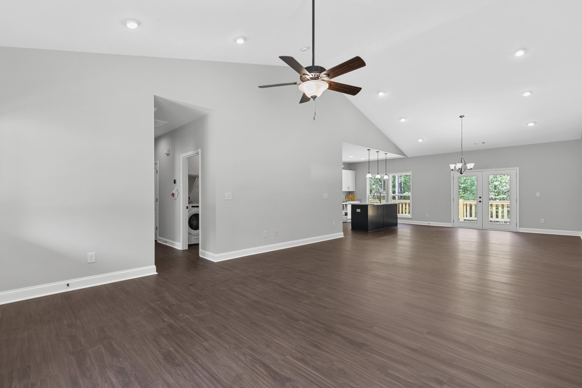 Spacious living room featuring wood flooring, white walls, ceiling fan with light fixture, white double doors with glass panes, and black kitchen island topped with marble